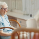 An elderly woman with dementia care at home, smiling warmly while seated in a rocking chair in a comfortable, sunlit room