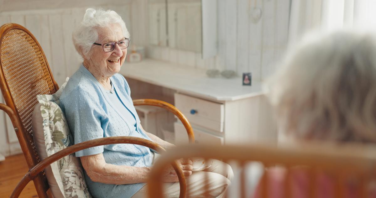 An elderly woman with dementia care at home, smiling warmly while seated in a rocking chair in a comfortable, sunlit room