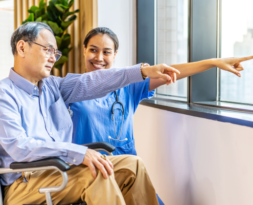 An Asian nurse comforting an elderly patient in a wheelchair, illustrating what is dementia training awareness in professional senior care facilities.