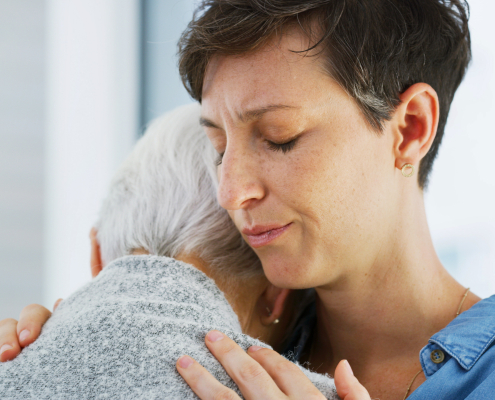 Woman hugging elderly mother in care home reflecting person-centred dementia training values of empathy and emotional support.
