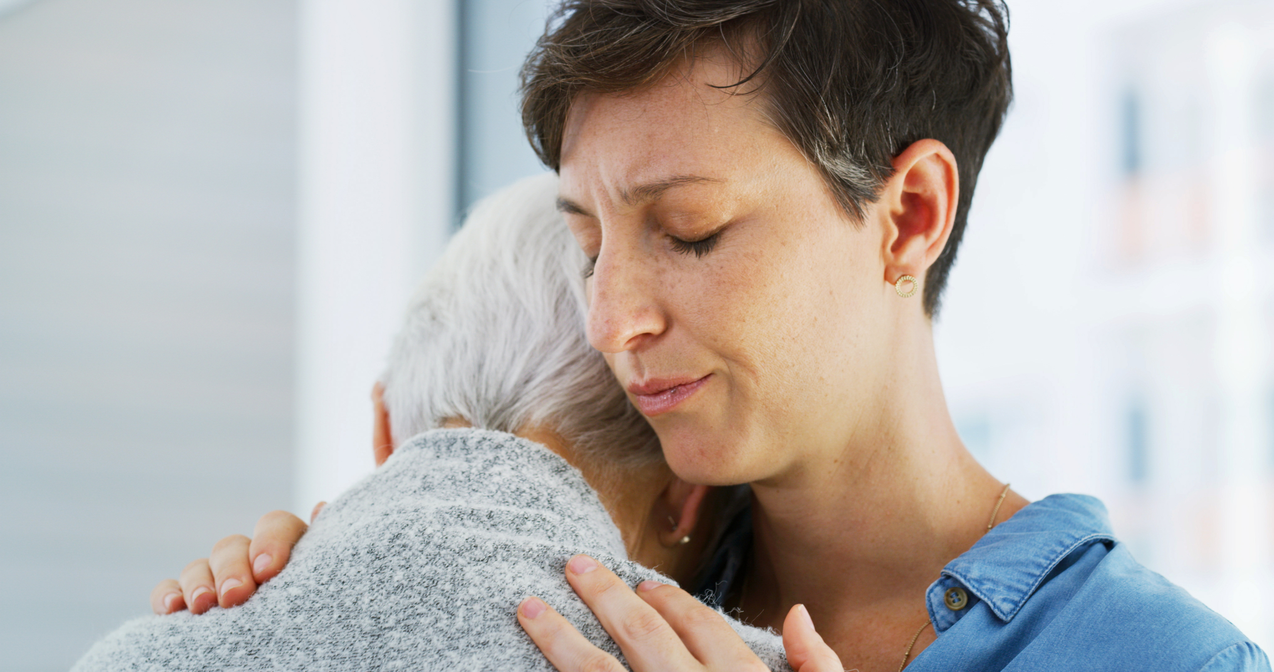 Woman hugging elderly mother in care home reflecting person-centred dementia training values of empathy and emotional support.