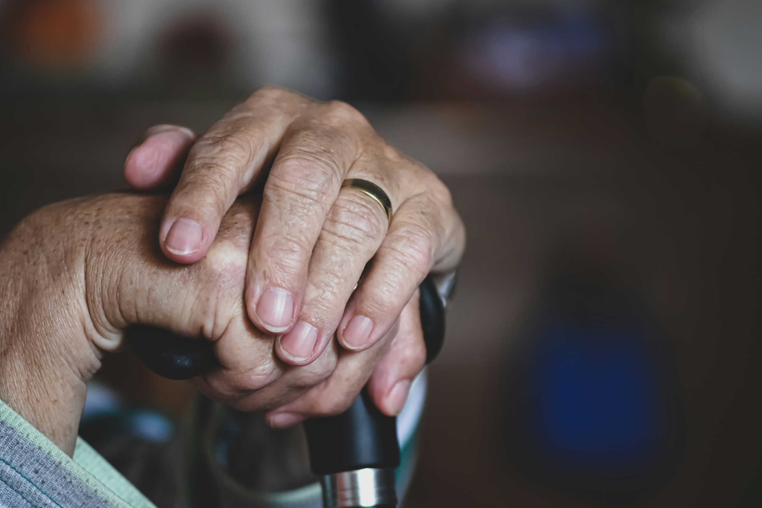 Wrinkled hands resting on the handle of a walking cane
